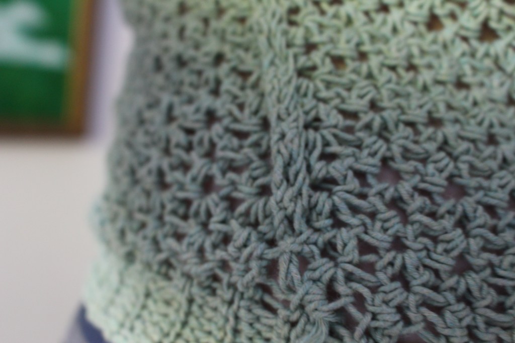 Close up of the side seam detail of a green crochet sweater near the bottom edge ribbing.