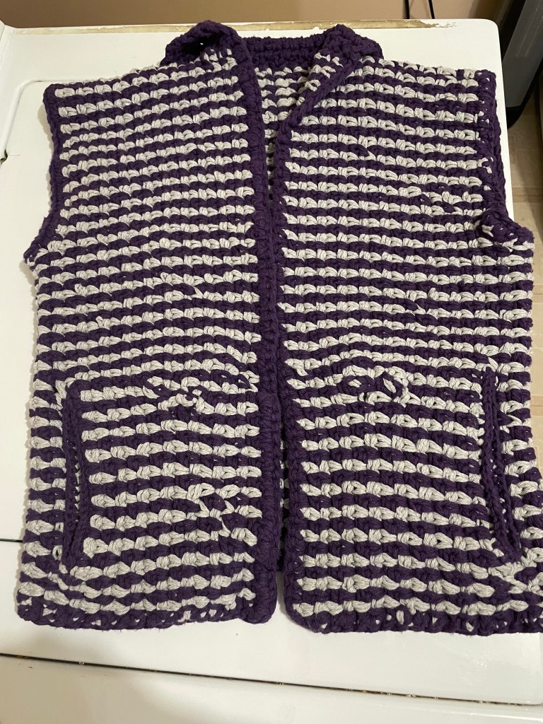 The front of a gray and purple striped crochet vest laying flat.