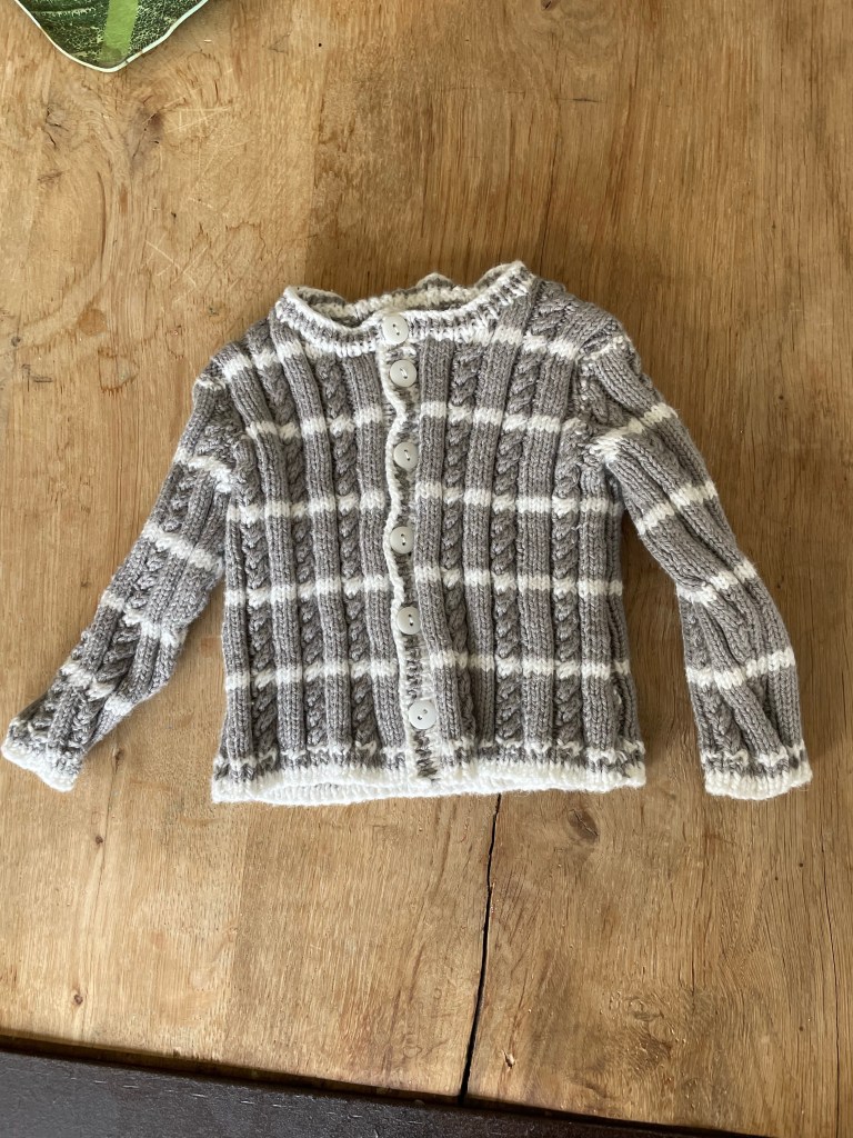 Front view of gray and white striped cable knit baby sweater with white buttons