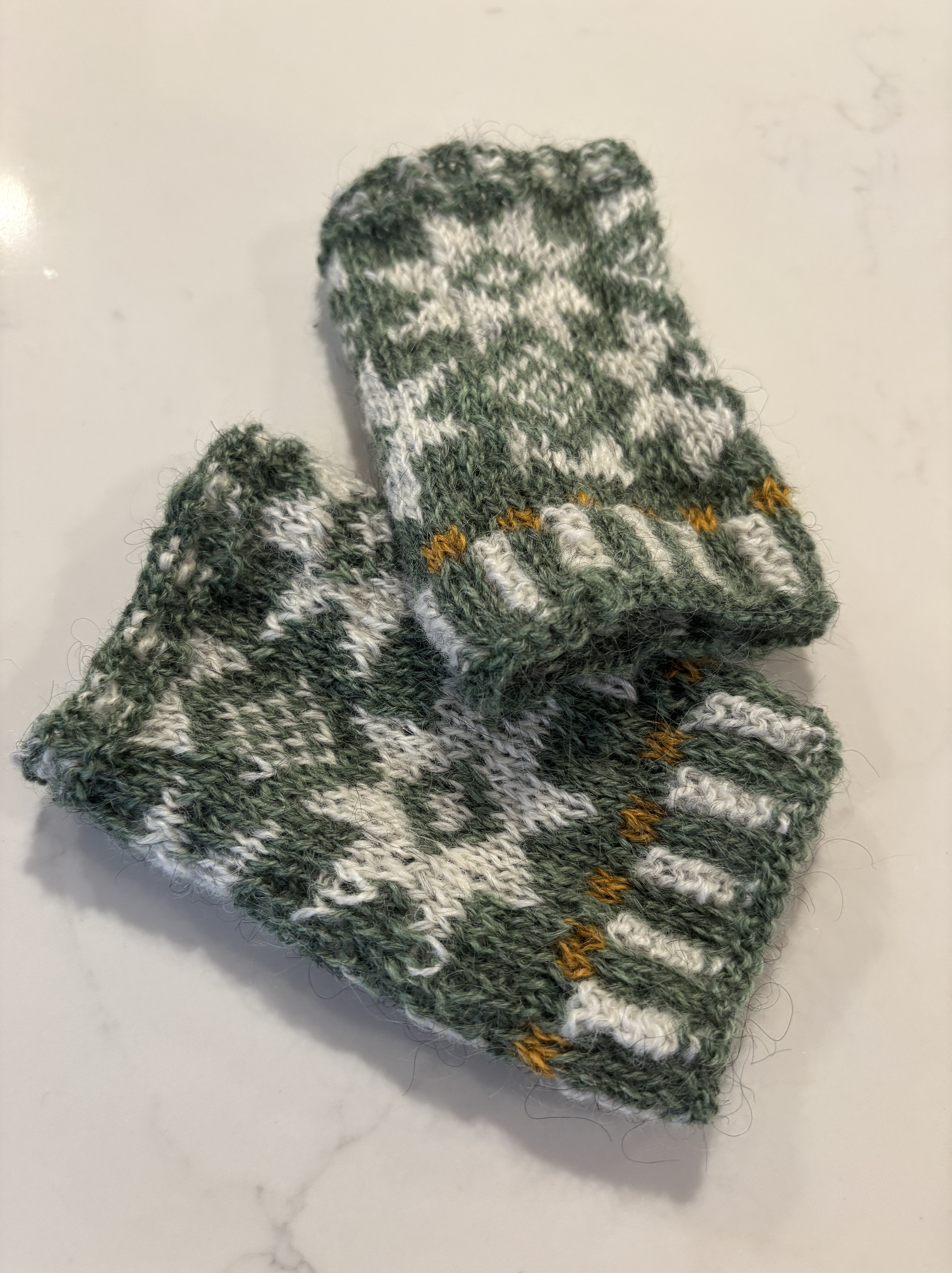 A pair of green knit rectangular wrist warmers with white star colorwork patterns