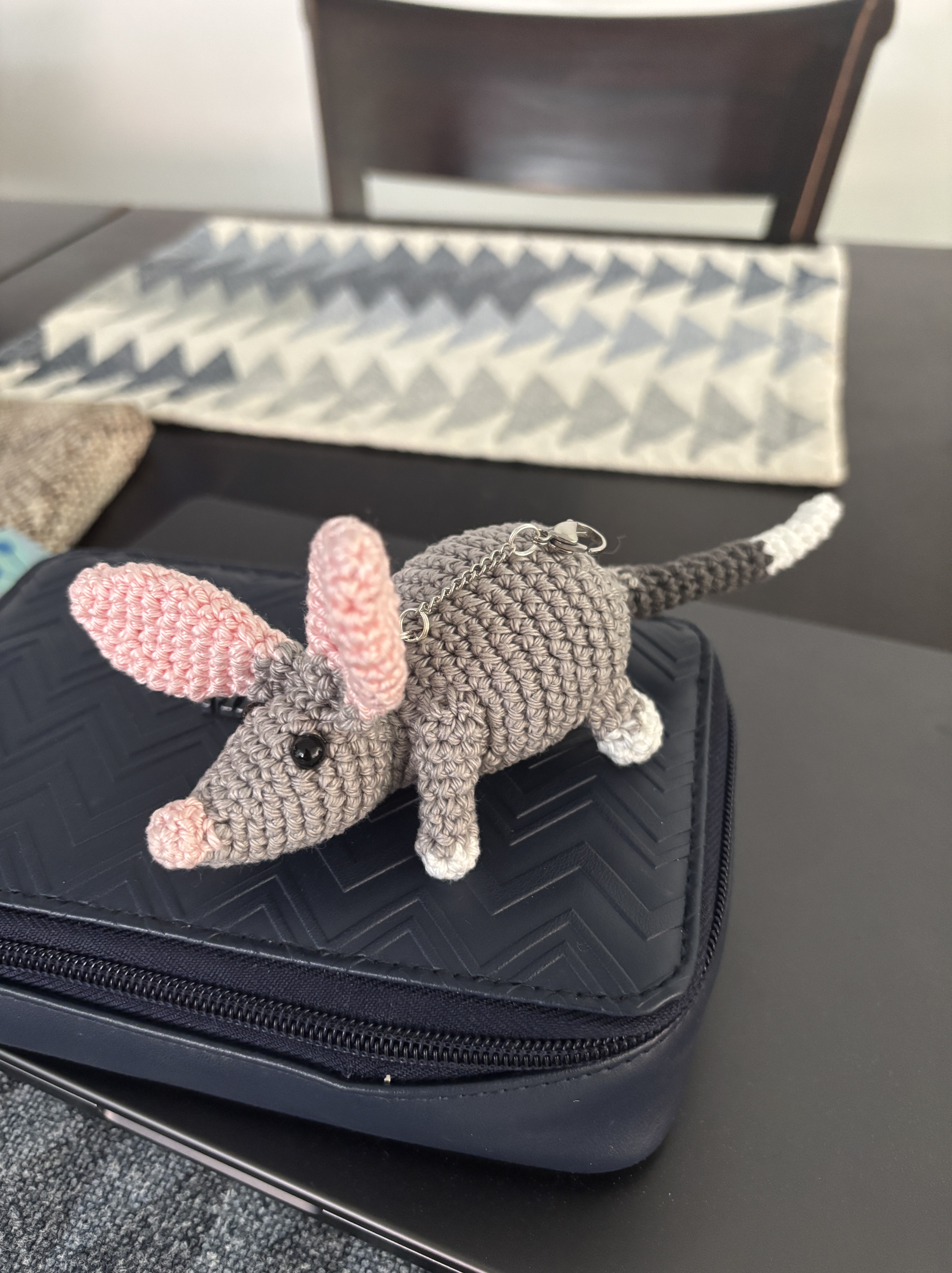 A gray crocheted bilby with pink ears and nose and white feet and tail tip